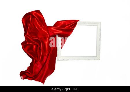 Tessuto satinato rosso volante che svela una cornice vintage bianca. Cornice di levitazione, mockup per presentazione o visualizzazione. Foto Stock