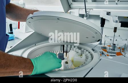 Laboratorio diagnostico scienziato nei guanti protettivi che lavora con analizzatore automatico biochimico del sangue, primo piano Foto Stock