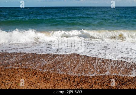 Un riassunto delle onde che si infrangono sulla spiaggia di ghiaia in estate in una brezza nord-orientale a Cley-Next-the-Sea, Norfolk, Inghilterra, Regno Unito. Foto Stock