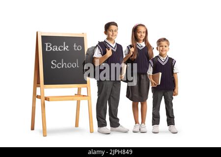 Scolari con zaini in piedi accanto a una lavagna su un piedistallo con testo di ritorno a scuola isolato su sfondo bianco Foto Stock