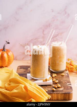 Un colpo verticale di due tazze di vetro di milkshakes di zucca con una paglia su un asse di legno Foto Stock