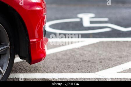 Auto rossa che attraversa il parcheggio per disabili Foto Stock