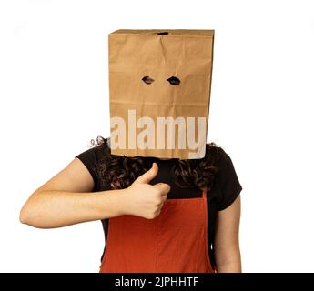 Giovane donna che indossa la borsa di carta sopra la testa con i pollici in su per approvazione Foto Stock