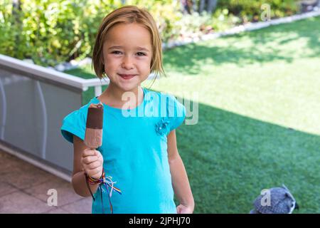 Ragazza sconosciuta, che indossa una t-shirt verde, con un gelato al cioccolato al latte, per strada, in estate, guardando la macchina fotografica. Gelato, papsiclo, eatina Foto Stock