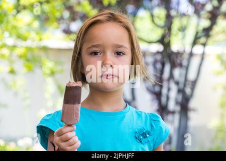 Ragazza sconosciuta, che indossa una t-shirt verde, con un gelato al cioccolato al latte, per strada, in estate, guardando la macchina fotografica. Gelato, papsiclo, eatina Foto Stock
