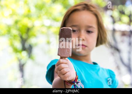 Ragazza sconosciuta, indossando una camicia verde. Fuori fuoco, tenendo un gelato al cioccolato al latte, messo a fuoco, per strada, in estate. Gelato, papsiclo, mangiare, s Foto Stock