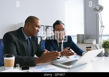 Imprenditori allegri che discutono le informazioni sullo schermo del laptop Foto Stock