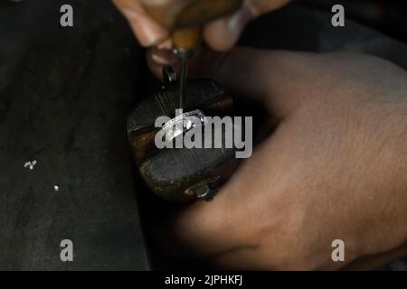 Primo piano di mano di un orafo che fissa il diamante sull'anello. Realizzazione di gioielli artigianali con strumenti professionali. Foto Stock