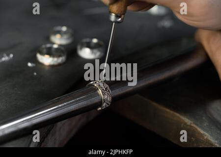 Primo piano di mano di un orafo che fissa il diamante sull'anello. Realizzazione di gioielli artigianali con strumenti professionali. Foto Stock