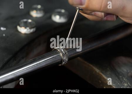 Primo piano di mano di un orafo che fissa il diamante sull'anello. Realizzazione di gioielli artigianali con strumenti professionali. Foto Stock