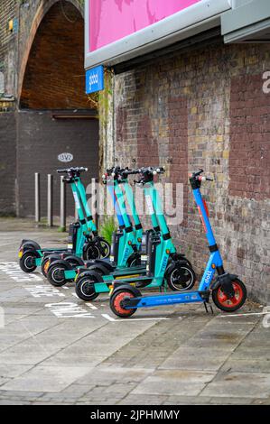 LONDRA - 20 maggio 2022: Scooter elettrici a noleggio allineati sul marciapiede accanto al vecchio muro di mattoni Foto Stock