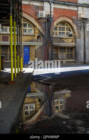 LONDRA - 20 maggio 2022: Vecchi edifici in mattoni della ferrovia ad arco a Waterloo riflesso in pouddle su strada Foto Stock