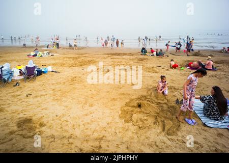 Scena animata sulla spiaggia di Scarborough durante un fine settimana estivo, con molte famiglie asiatiche in acqua e sulla sabbia Foto Stock