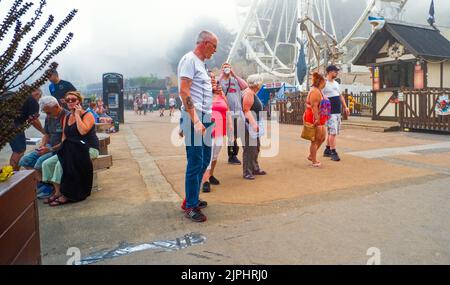 Persone in un gruppo di famiglia vicino alla grande ruota in una giornata di misty in estate a Scarborough, North Yorkshire Foto Stock