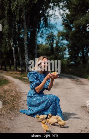 Bella giovane bionda in un abito blu nel bosco con anatroccoli Foto Stock