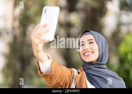 Donna musulmana che prende un selfie in un parco Foto Stock