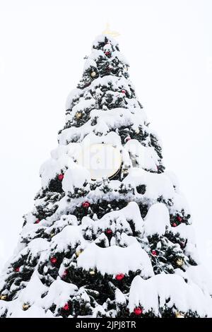 Albero di Natale sotto la neve all'aperto sullo sfondo di un cielo nuvoloso. Le mani sull'orologio a cinque a dodici Foto Stock