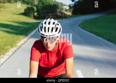 Giovane donna professionista bicyclist durante la corsa su strada, movimento continuo con massimo sforzo, vista ravvicinata. Foto Stock