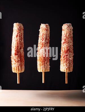 Elotes Callejeros sono uno spuntino di strada popolare in Messico, è grano tenero cucinato con spezie, spiedato su un bastone di legno coperto di maionese o così Foto Stock