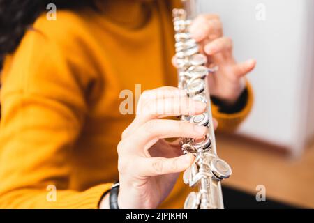 Primo piano di una donna irriconoscibile con un maglione giallo, che gioca un flauto trasversale. Foto Stock