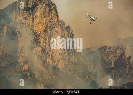 Un elicottero Ranger vola sulle montagne in fiamme. In una giornata con più di 40 gradi di temperatura e un forte vento scirocco, un grande incendio ha bruciato quasi 100 ettari di montagne nei dintorni del paese turistico di Scopello. Alcune case della gente del posto e dei turisti sono state evacuate. L'incendio fu fermato prima di iniziare a bruciare la riserva naturale dello Zingaro, la prima dichiarata in Sicilia nel 1981. Due Canadair, due elicotteri, uno dalla guardia forestale e uno dall'esercito, insieme a diversi gruppi di terra della guardia forestale sono riusciti a fermare il fuoco prima della notte. (Foto di Antonio Cascio/SO Foto Stock