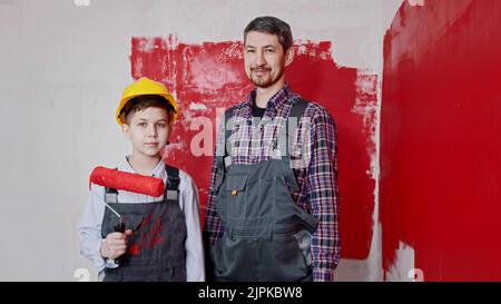 Un ragazzino e suo padre in piedi nella stanza e tenendo i rulli per la pittura a muro. Scatto medio Foto Stock