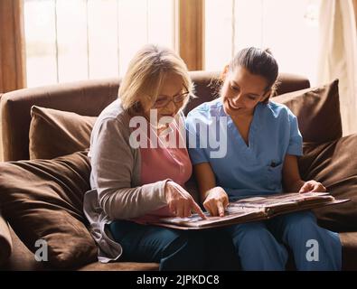 Scatenando alcuni vecchi ricordi, un'infermiera e una donna anziana che guardano insieme un album fotografico. Foto Stock