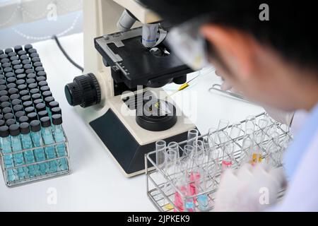 Immagine ravvicinata, scienziato asiatico maschio concentrato o chimico che lavora in laboratorio, regolare un nuovo campione liquido in una provetta. Foto Stock