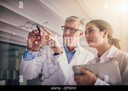 Iniziamo da qui. Due scienziati concentrati che lavorano insieme risolvendo equazioni su una parete di vetro in un laboratorio. Foto Stock