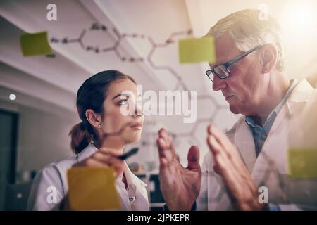 Iniziamo piccolo ma pensiamo in grande. Due scienziati concentrati che lavorano insieme risolvendo equazioni su una parete di vetro in un laboratorio. Foto Stock