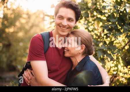 Felice figlio abbracciando la madre sorridente all'aperto in estate Foto Stock