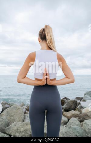 Vista posteriore di una ragazza che fa yoga sulla riva del mare. Foto Stock