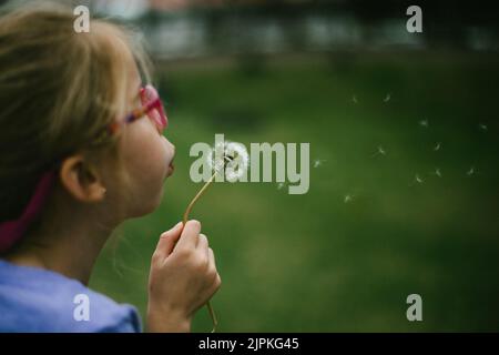 Ragazza bionda bambino soffia un dente di leone su erba verde Foto Stock