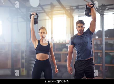 Una coppia di fitness che fa un allenamento con kettlebell, un esercizio fisico o un allenamento in palestra. Adatta le persone sportive, donna o uomo con una presa forte, esercitandosi con la gyming Foto Stock