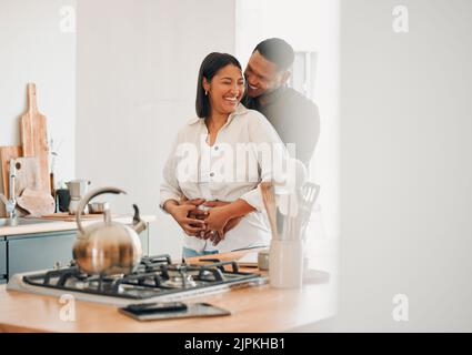 Coppia amorevole, felice e abbracciante rilassarsi in cucina a casa sorridendo e ridendo insieme. Gli amanti spensierati, eccitati e affettuosi che si divertono Foto Stock