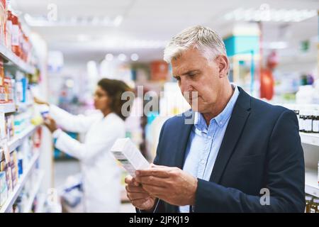 Mi chiedo se questo è il roba di destra. Un uomo maturo ben vestito che naviga gli scaffali di una farmacia che cerca il giusto farmaco da comprare. Foto Stock