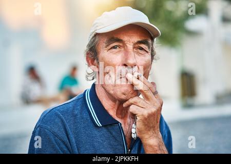 Trascinare. Ritratto di un uomo anziano allegro che fuma una sigaretta e che sta fuori mentre guarda la macchina fotografica. Foto Stock