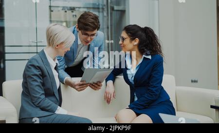 Allegro uomo d'affari che parla e discute di rapporto finanziario con colleghi di lavoro donne seduti sul divano in sala riunioni al coperto Foto Stock