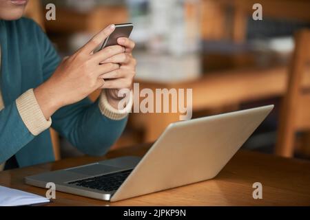 Immagine ritagliata di un uomo che controlla il telefono quando lavora su un computer portatile Foto Stock