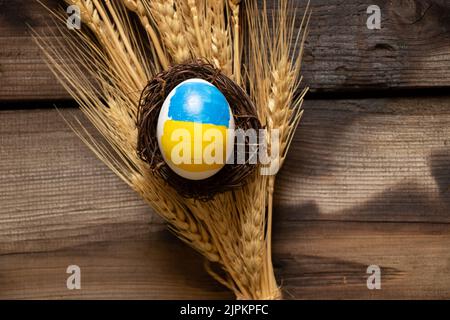 Un uovo di pollo bianco con una bandiera dipinta di Ucraina in un cesto di paglia è sulle orecchie di grano, cultura e vacanze 2022, raccolto in Ucraina Foto Stock