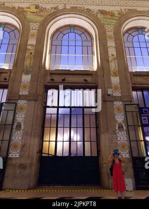 Interno della stazione ferroviaria di Sao Bento a Porto, Portogallo di notte. Una turista femminile scatta una foto accanto a una delle porte. Foto Stock