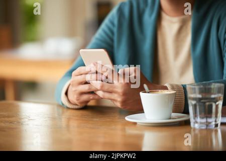 L'uomo legge le notizie sul suo telefono quando beve il caffè di mattina Foto Stock