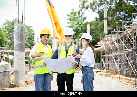 Un team di giovani ingegneri civili asiatici di talento che guardano il progetto e lavorano insieme nel cantiere. Foto Stock