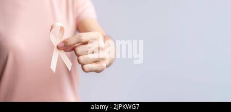 Donna mano che tiene il nastro di Peach per il mese di settembre di consapevolezza del cancro uterino. Sanità e concetto di giornata mondiale del cancro Foto Stock