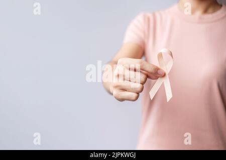 Donna mano che tiene il nastro di Peach per il mese di settembre di consapevolezza del cancro uterino. Sanità e concetto di giornata mondiale del cancro Foto Stock