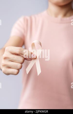 Donna mano che tiene il nastro di Peach per il mese di settembre di consapevolezza del cancro uterino. Sanità e concetto di giornata mondiale del cancro Foto Stock