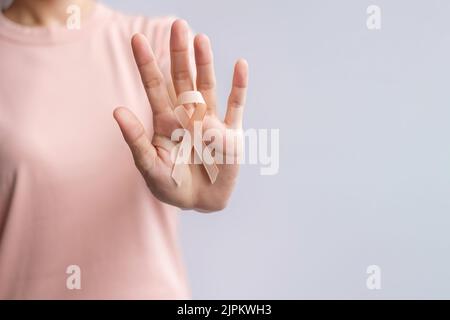 Donna mano che tiene il nastro di Peach per il mese di settembre di consapevolezza del cancro uterino. Sanità e concetto di giornata mondiale del cancro Foto Stock