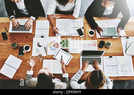 Overhead dei colleghi che hanno una riunione di marketing in un ufficio moderno. Al di sopra di un luogo di lavoro occupato, i colleghi si scambiano idee e sviluppano strategie per una startup Foto Stock