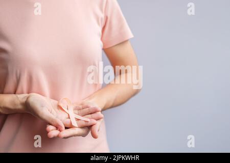 Donna mano che tiene il nastro di Peach per il mese di settembre di consapevolezza del cancro uterino. Sanità e concetto di giornata mondiale del cancro Foto Stock