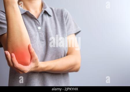 donna adulta con dolore muscolare su sfondo grigio. Donna che ha dolori al gomito a causa di epicondilite laterale o gomito da tennis. Lesioni e conce medico Foto Stock